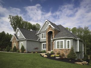 Large, suburban home with green lawn, grey siding, and stone siding